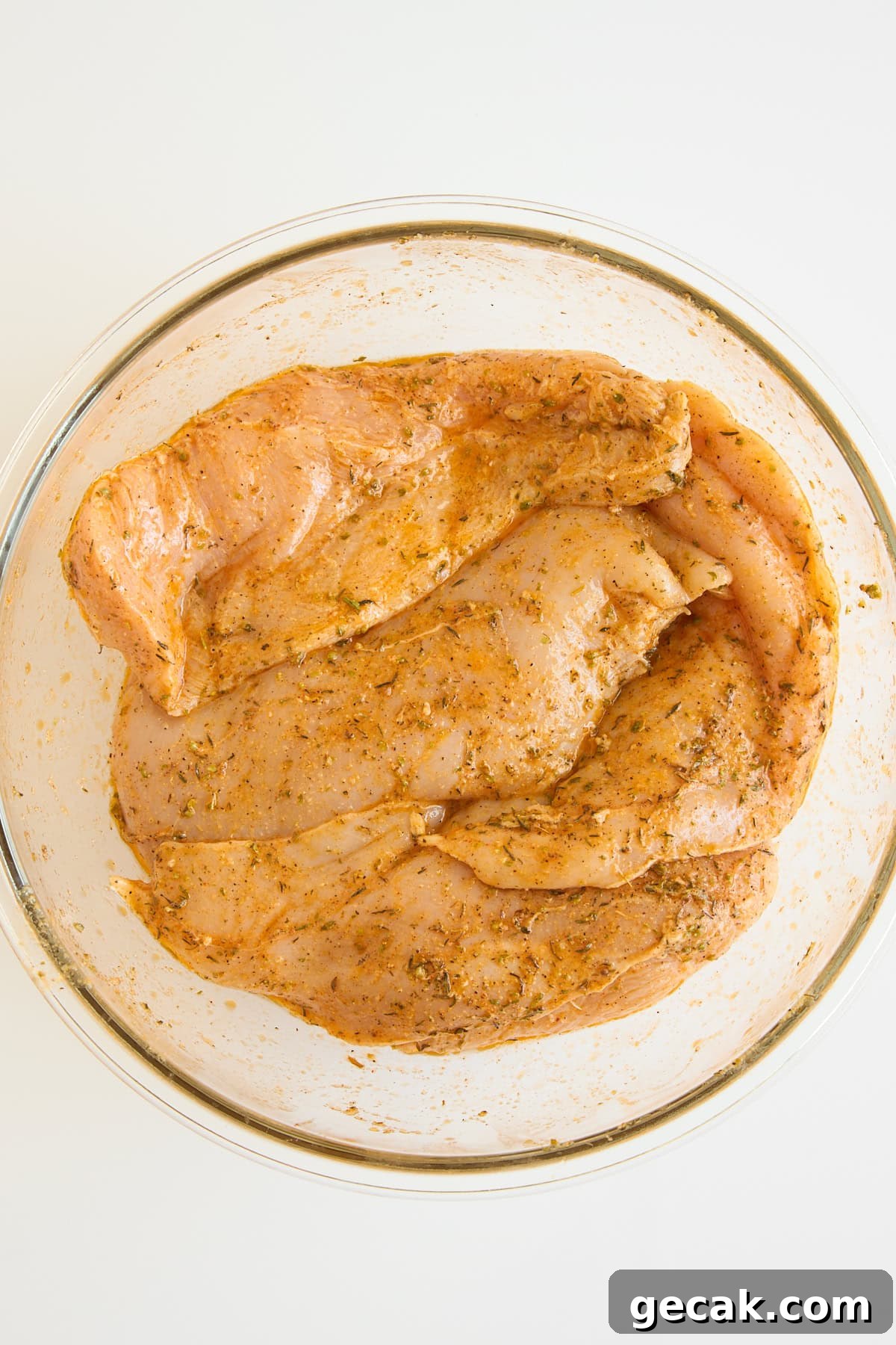 Raw chicken breasts marinating in a bowl. 