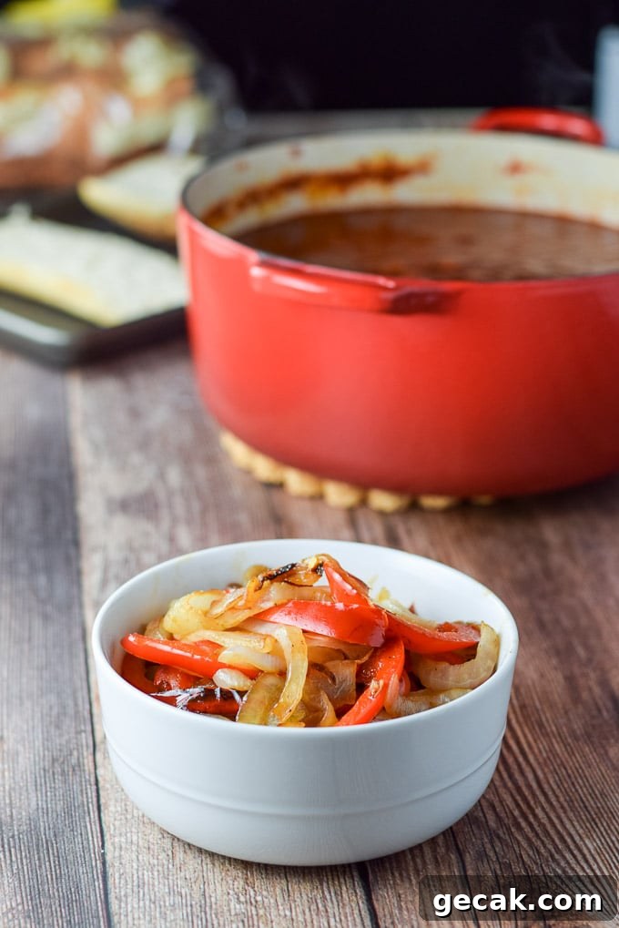 Onion and pepper cooked and in a little bowl. There is a red Dutch oven filled with red gravy in the background