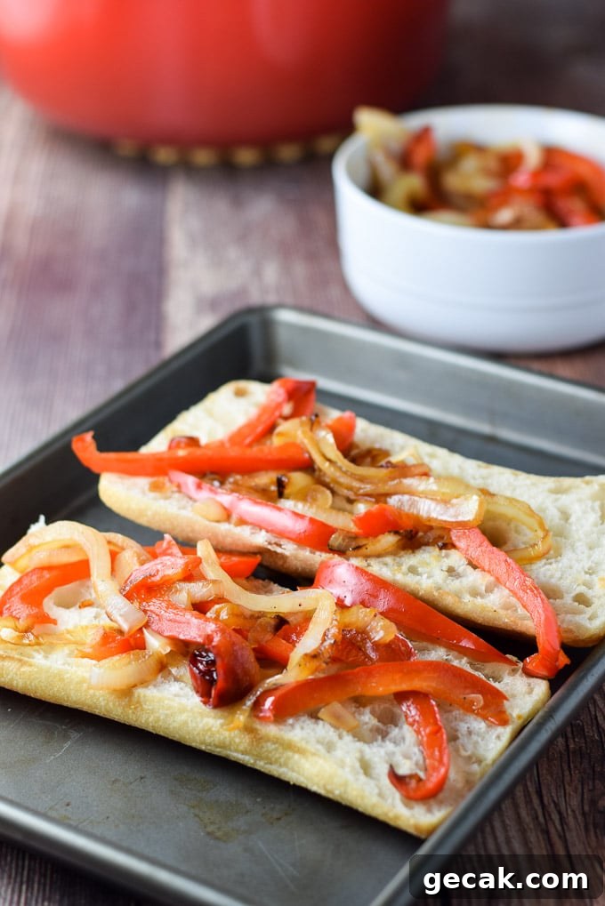 Onion and pepper on a sub roll on the pan with the veggies in a bowl behind it