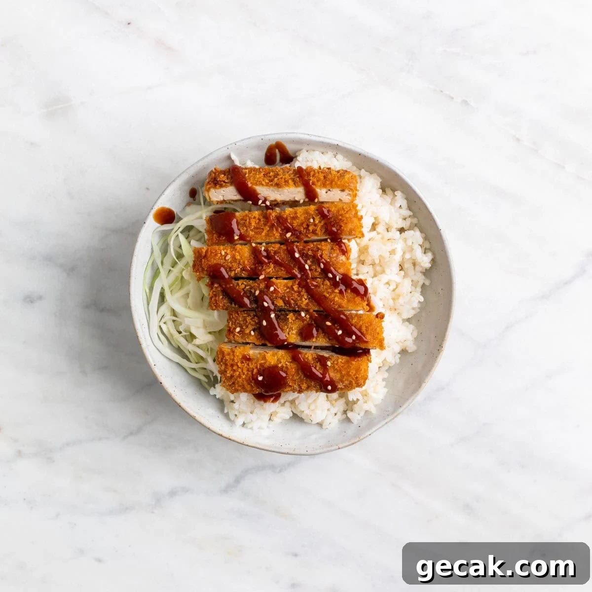 Bowl of tofu katsu served over rice with cabbage on the side and sesame seeds on top.