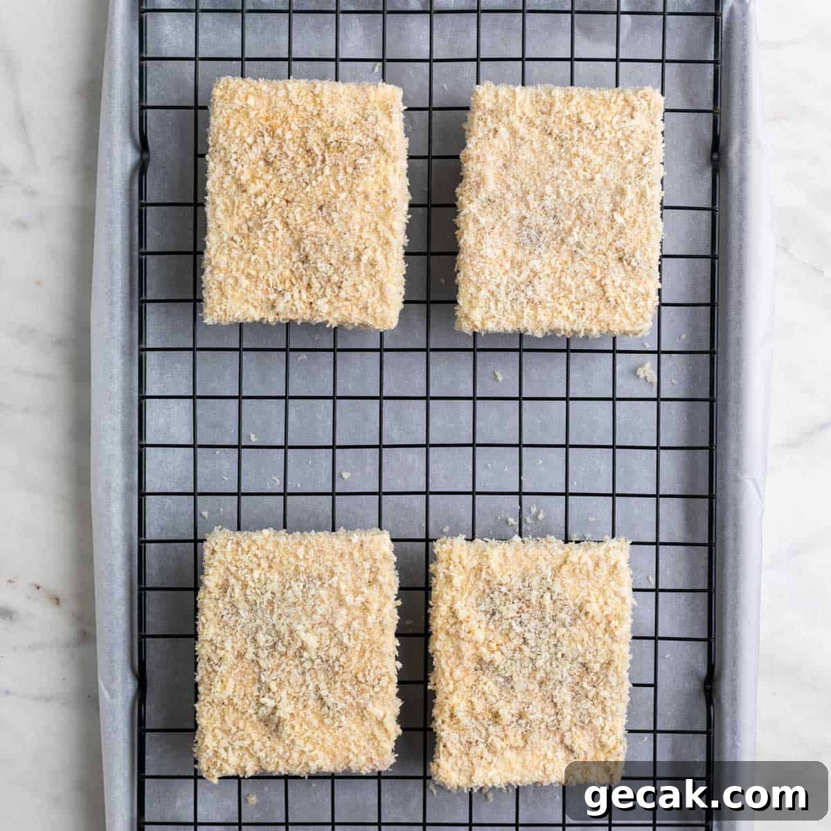 Breaded tofu pieces on a wire rack on a lined baking sheet before cooking.