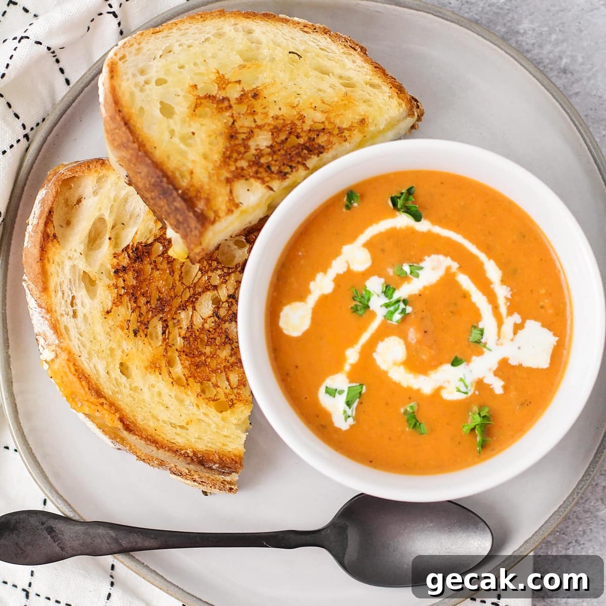 Tomato basil soup in bowl with grilled cheese on plate.