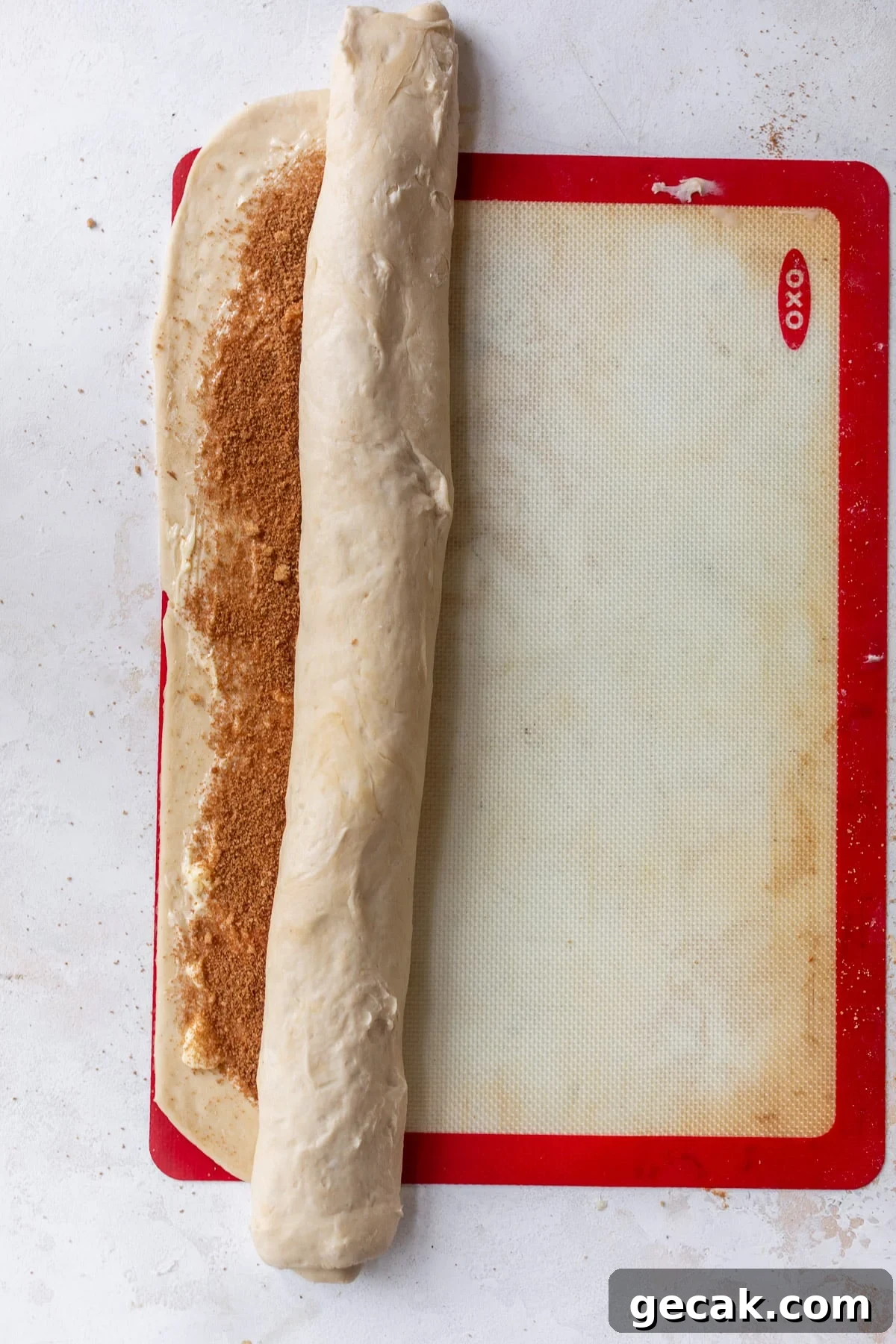 overhead view of a half-rolled log of vegan cinnamon roll dough on a baking mat.
