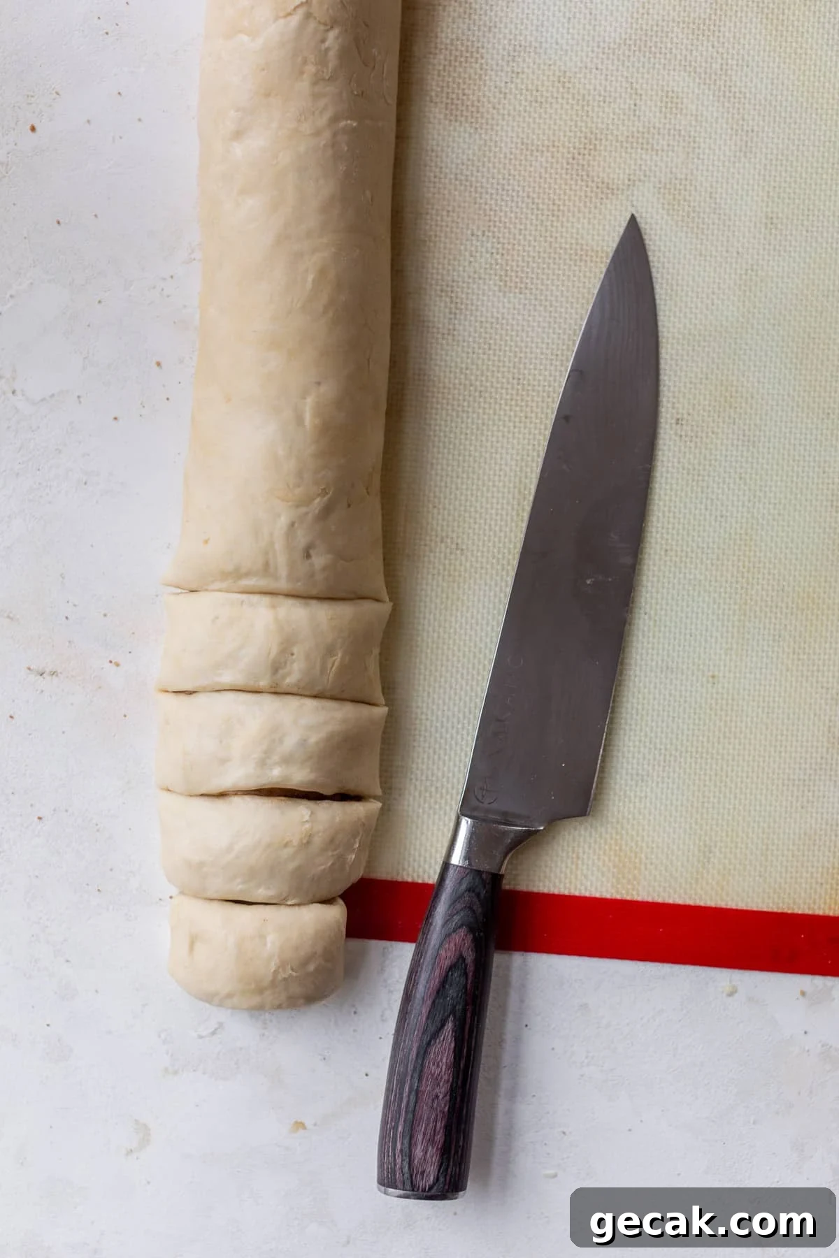 overhead view of a chef's knife next to a log of vegan cinnamon roll dough on a baking mat.