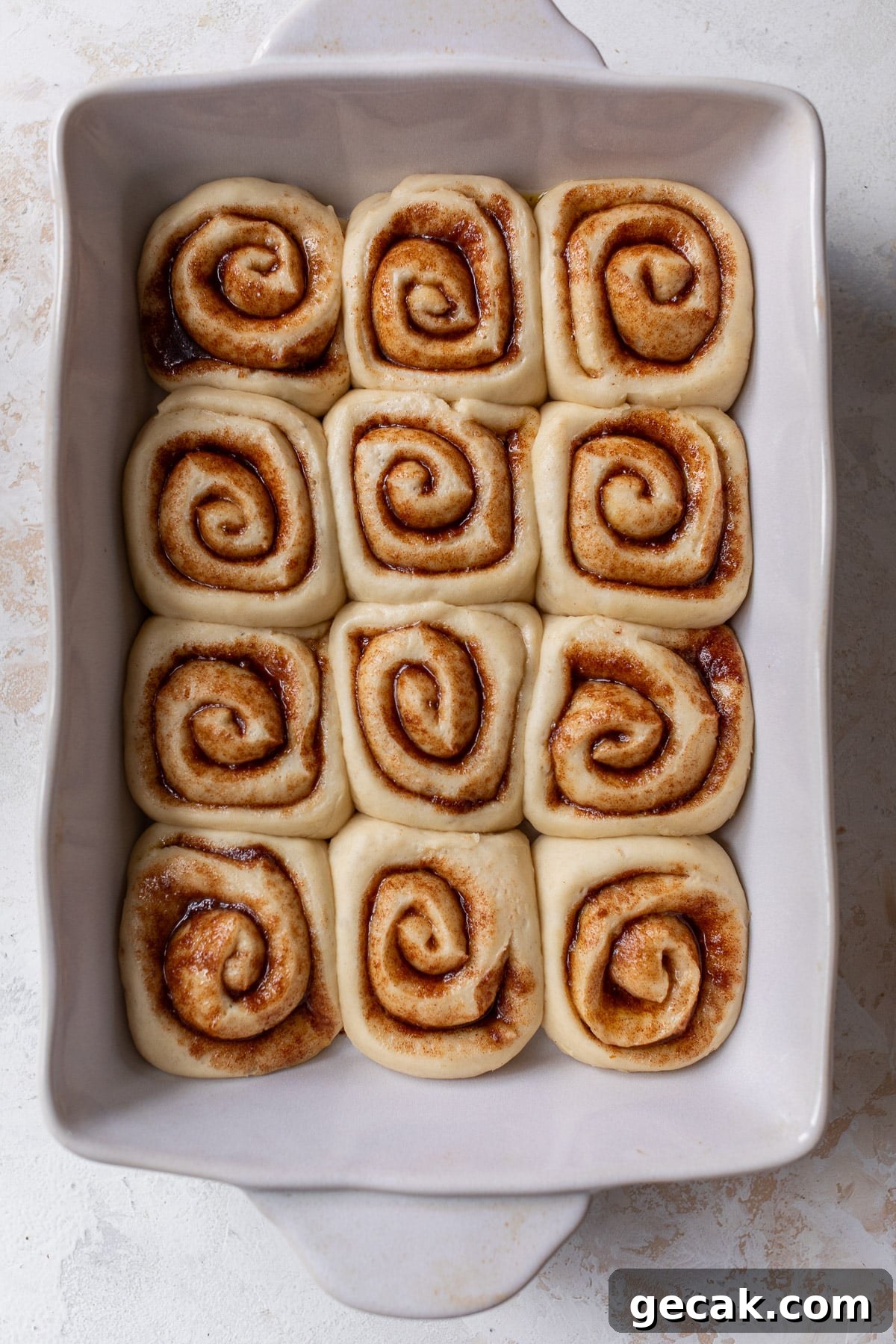 overhead view of risen and unbaked vegan cinnamon rolls in a white baking dish.