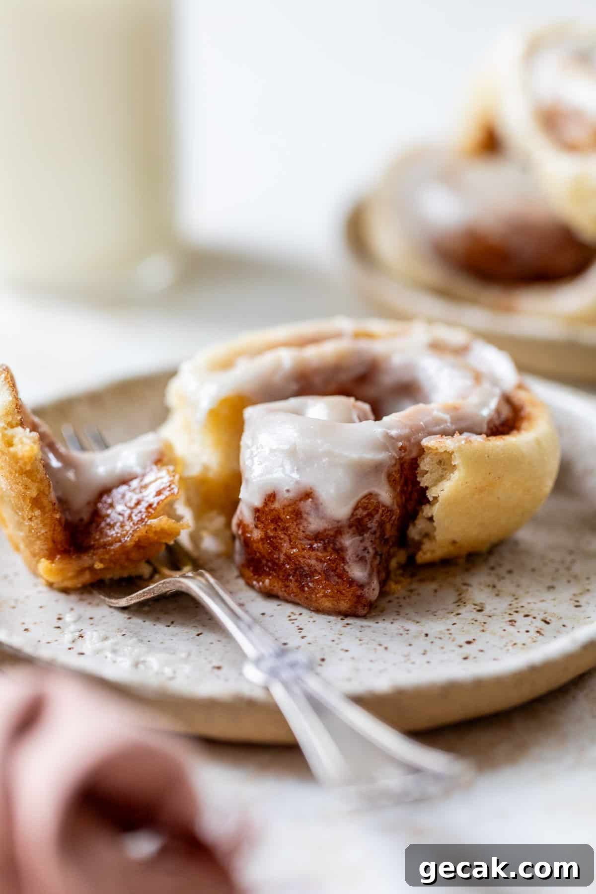 side view of a fork next to a cream cheese frosting-topped vegan cinnamon roll on a plate.