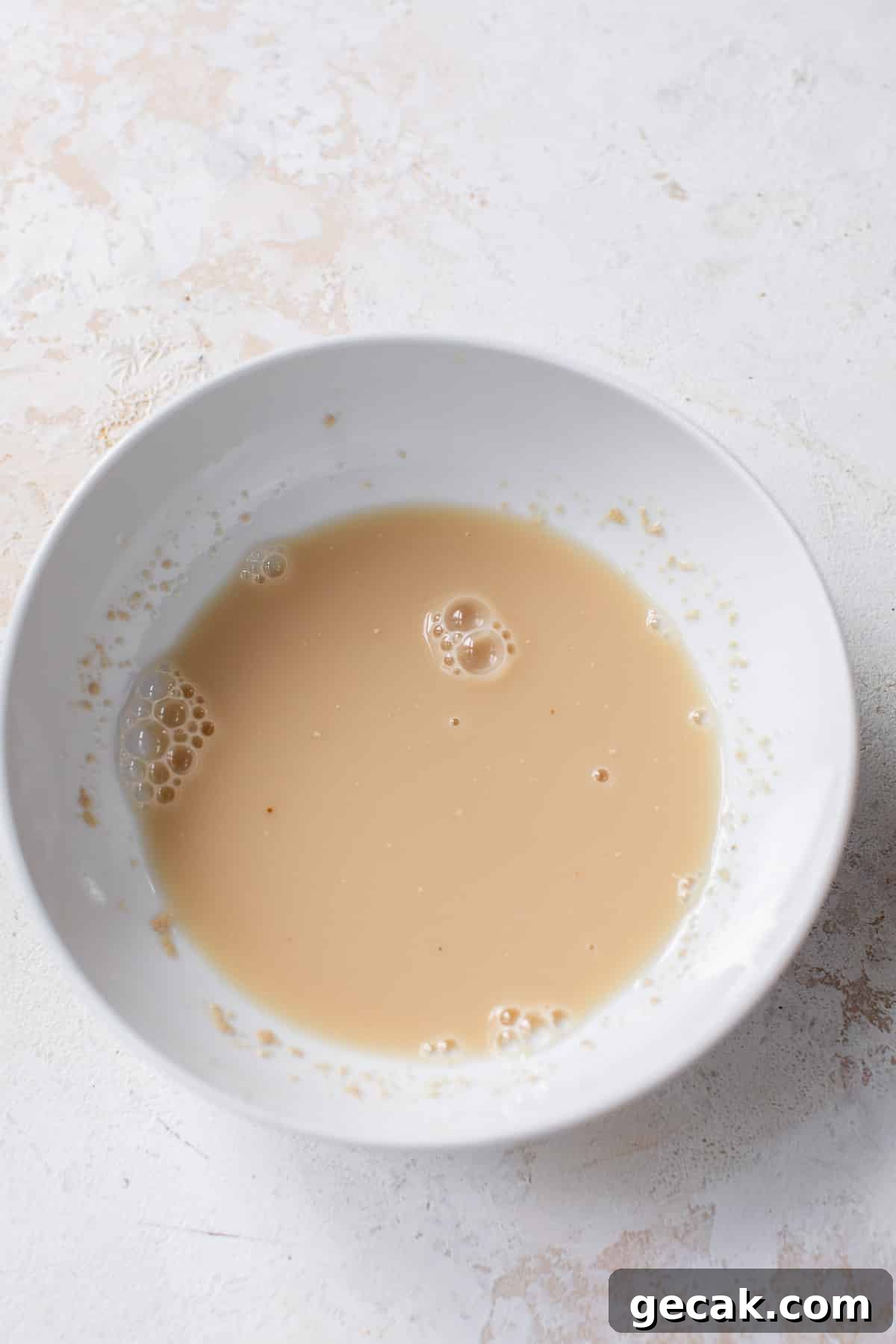 overhead view of a liquid yeast mixture for vegan cinnamon rolls in a white bowl.