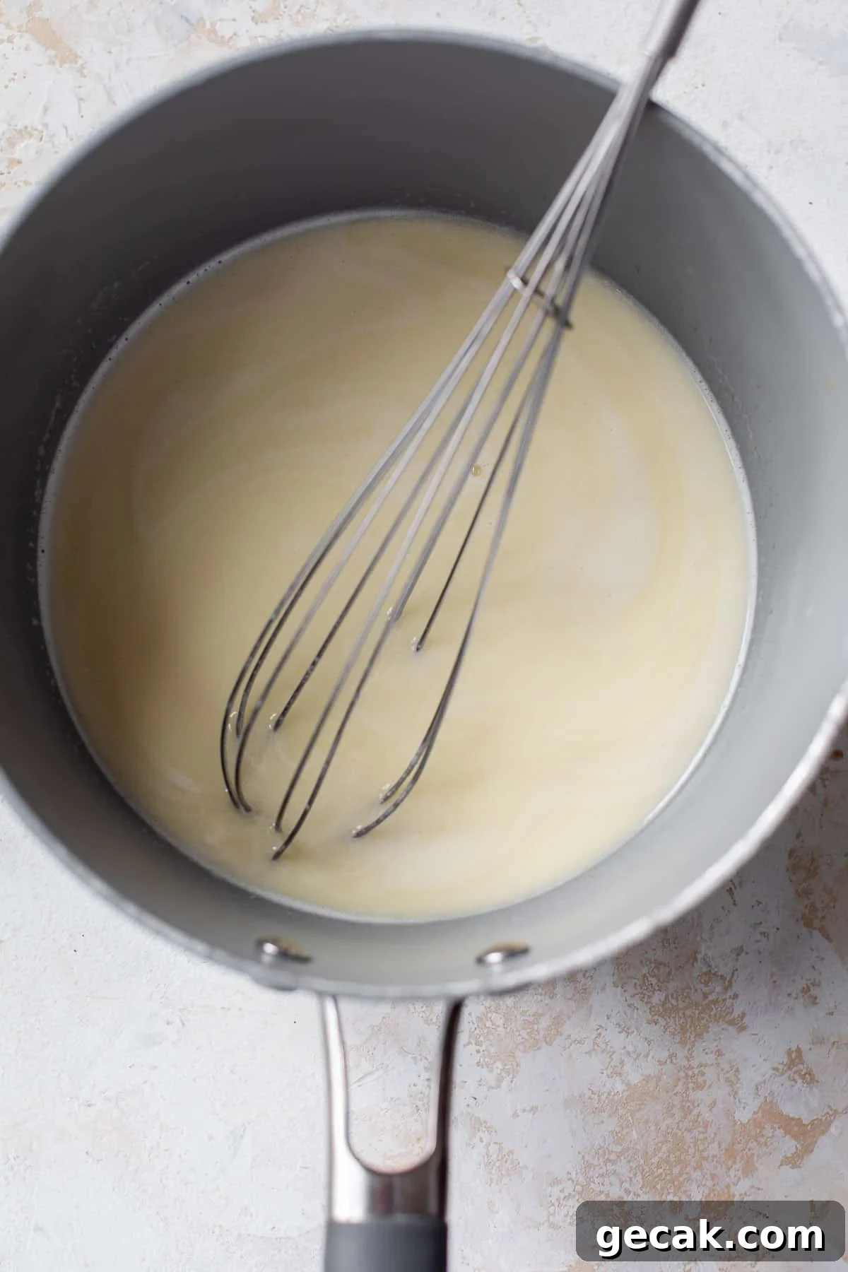 overhead view of a whisk in a liquid butter-milk mixture for vegan cinnamon rolls in a saucepan.
