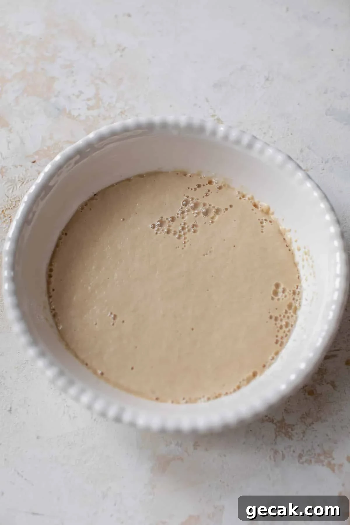 overhead view of a bubbly yeast mixture for vegan cinnamon rolls in a white bowl.
