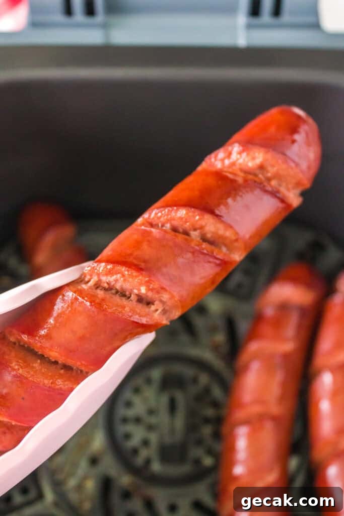 Crispy Air Fryer Hot Dogs: Quick, Juicy, and Ready in Minutes 7 Tongs lifting a fully cooked scored hot dog from the air fryer