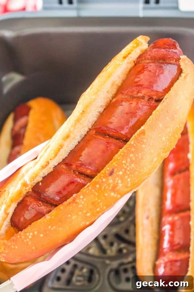 Crispy Air Fryer Hot Dogs: Quick, Juicy, and Ready in Minutes 9 Tongs holding a crispy hot dog in a toasted hoagie bun