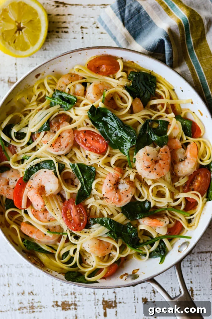 A skillet of shrimp scampi with tomatoes and spinach.
