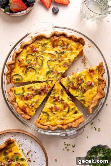 Bacon and roasted jalapeño Quiche in a pie dish sliced and topped with chives and crumbled bacon.