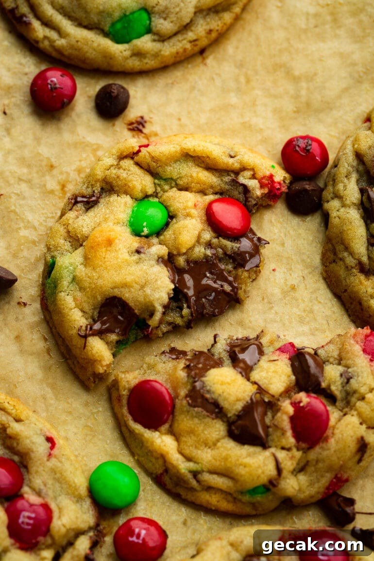 a photo of a golden baked chocolate chip m&m Christmas cookie that has been broken in half so you can see the gooey middle.