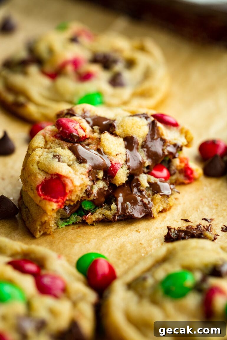 a photo of a thick and chewy chocolate chip with Christmas m&m's that has been broken in half and stacked on top of each other so you can see the gooey inside.