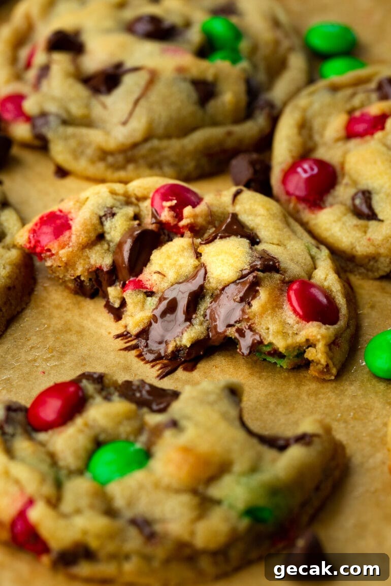 a photo of a gooey chocolate chip m&m cookie that has been broken in half and pulled apart to see the melted chocolate chips.