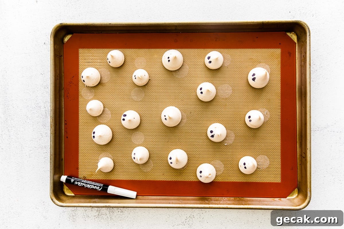 Ghost meringues lined up on a baking sheet, dotted with eyes.