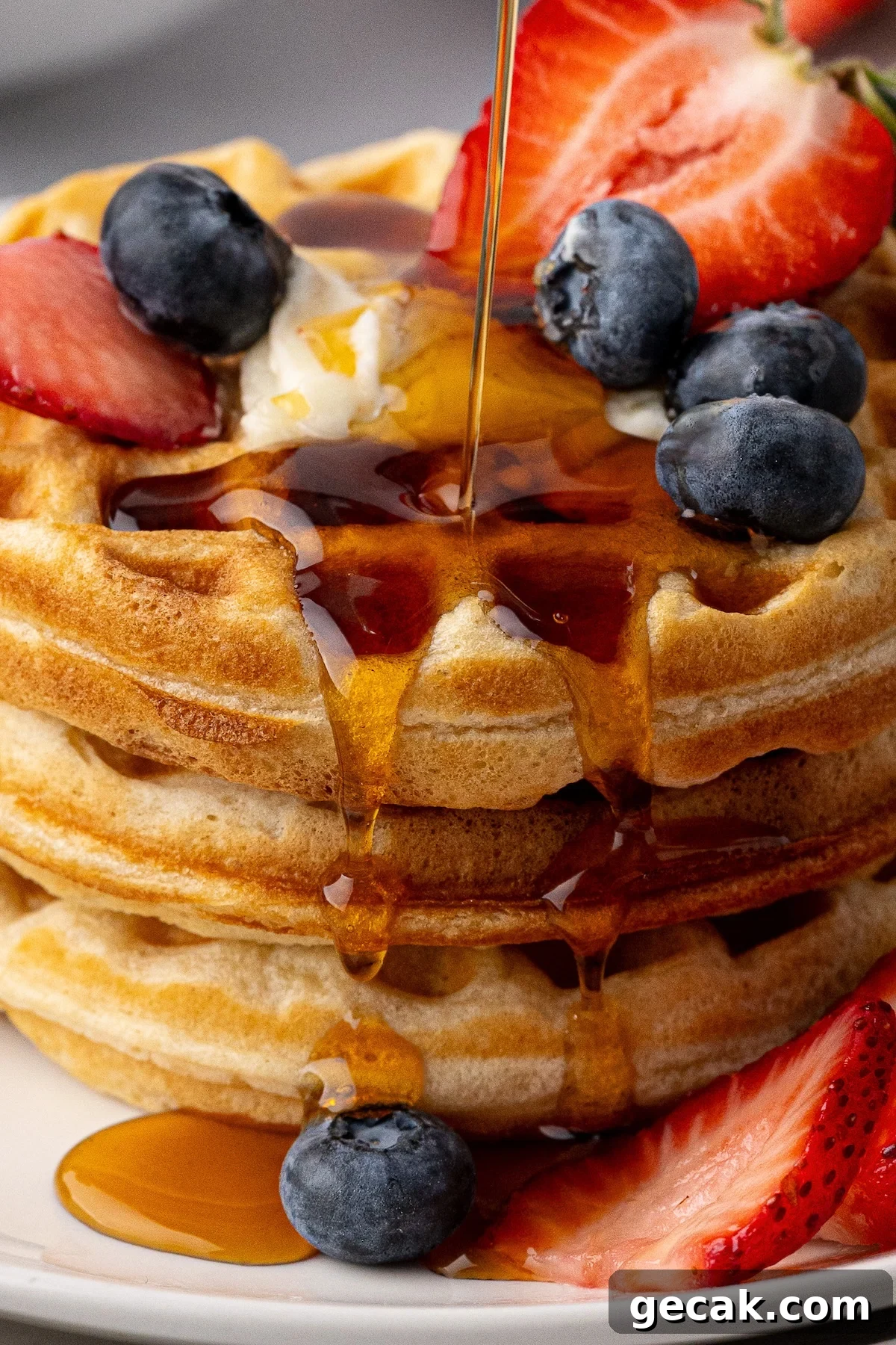 Maple syrup being poured over a stack of thick Southern-style buttermilk waffles.
