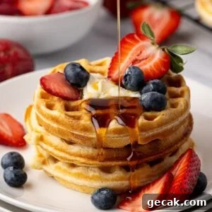 Maple syrup being poured on a stack of thick and fluffy buttermilk waffles, garnished with fresh berries.