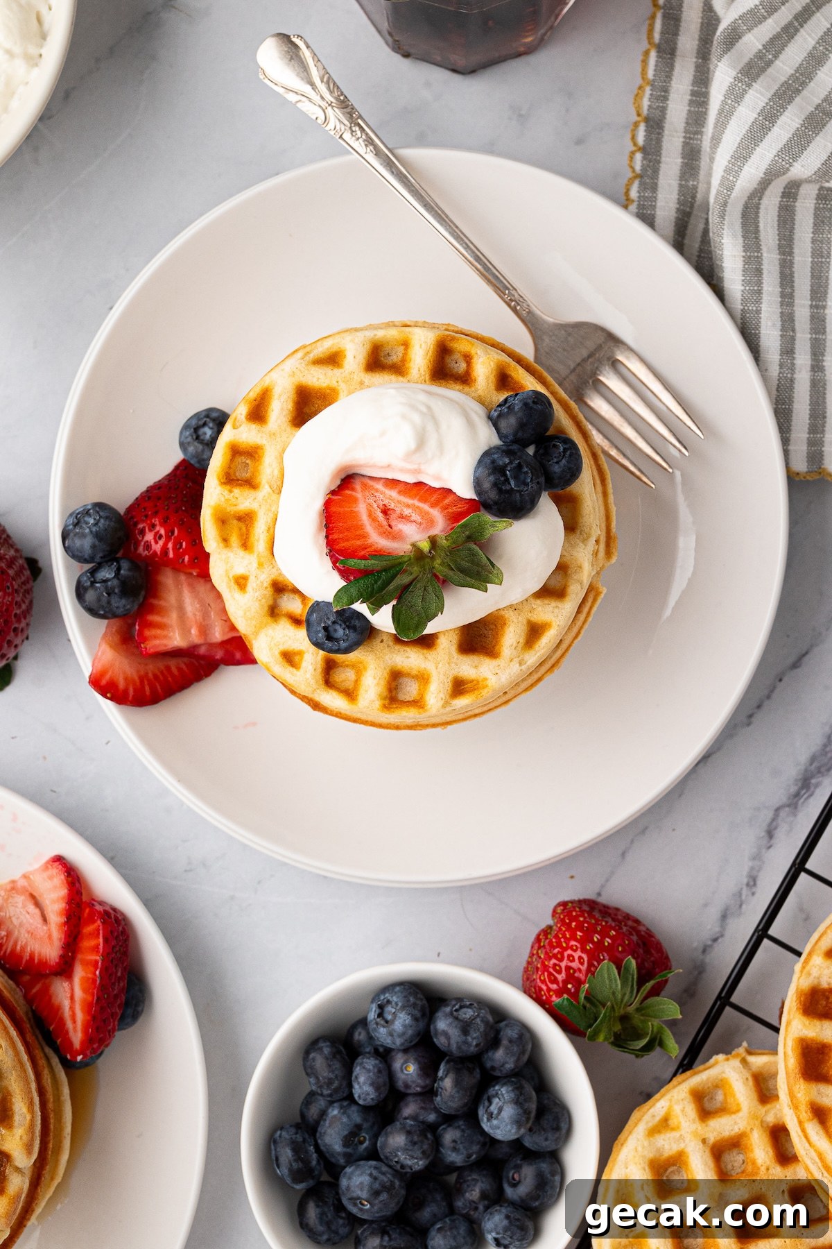 Golden brown buttermilk waffles on a white plate served with maple syrup, cream and fresh berries.