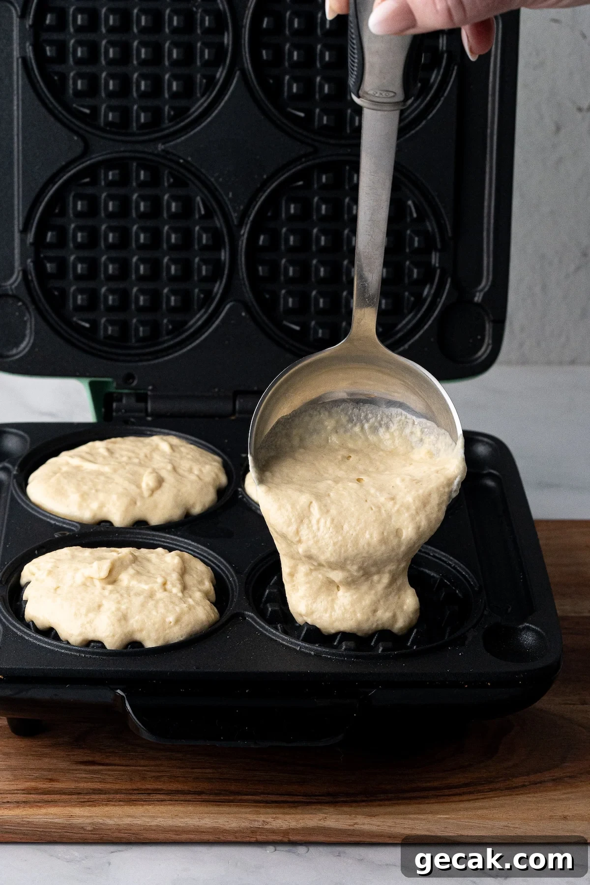 Pouring thick homemade waffle batter into a preheated waffle iron to cook.
