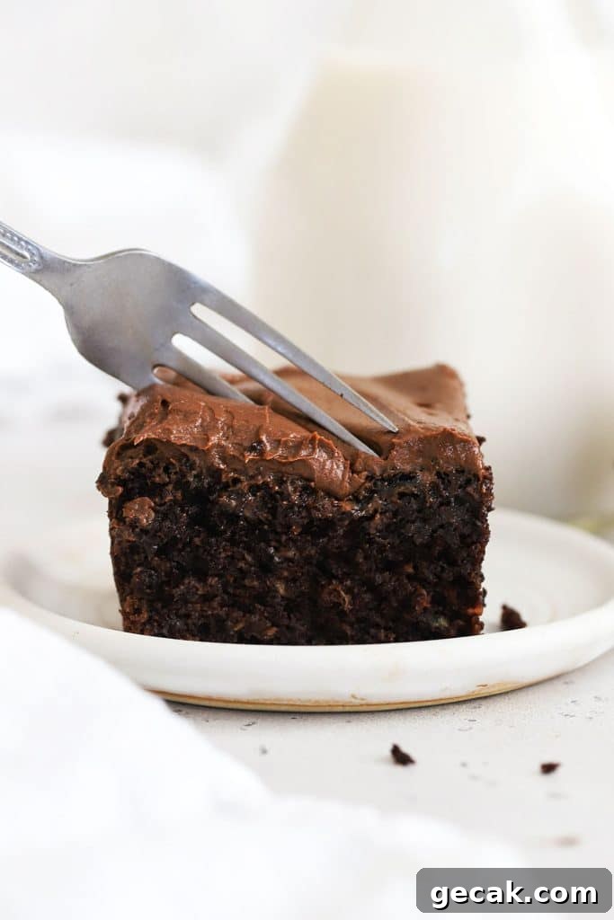 a fork cutting into a slice of gluten-free chocolate zucchini cake with chocolate frosting