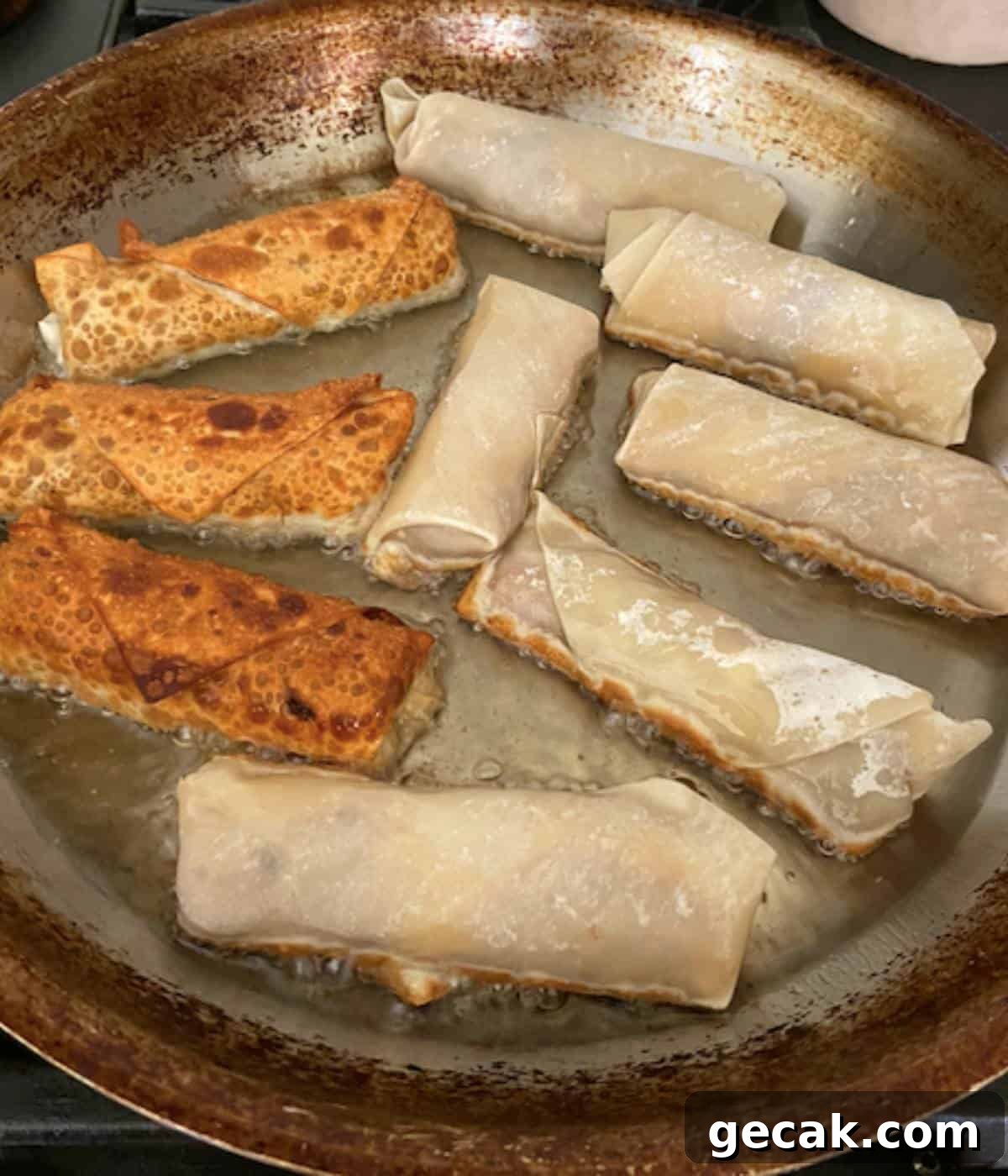 BBQ Pulled Pork Egg Rolls (Southern-Style Redneck Egg Rolls) 10 Egg rolls frying in vegetable oil in skillet.