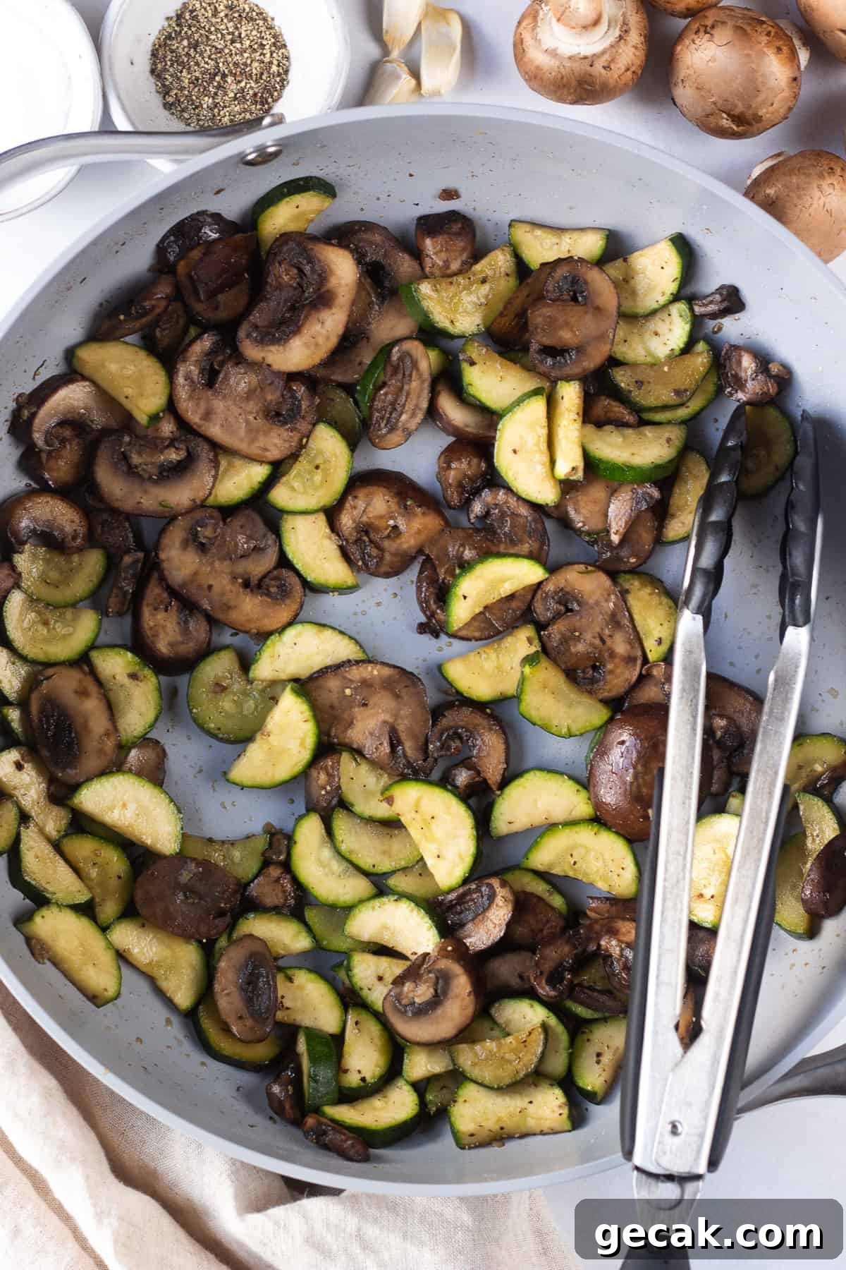 20-Minute Sautéed Zucchini and Mushrooms Recipe 2 top down shot of sauteed mushrooms and zucchini in a gray pan with tongs resting on the side.