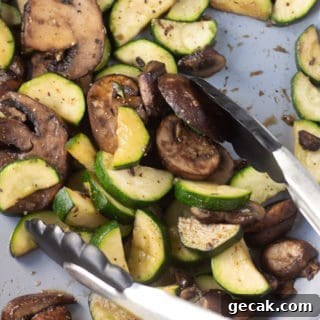 20-Minute Sautéed Zucchini and Mushrooms Recipe 11 Zucchini and mushrooms in a gray pan being stirred with black tongs.