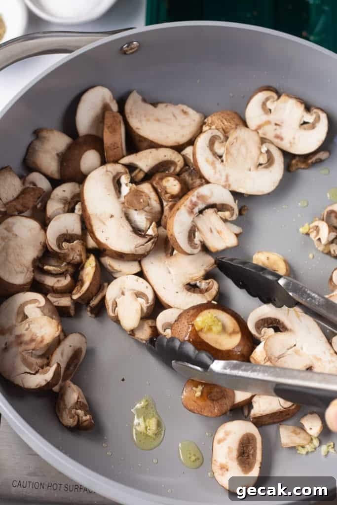 20-Minute Sautéed Zucchini and Mushrooms Recipe 5 sliced mushrooms being stirred into oil and garlic in a gray pan.