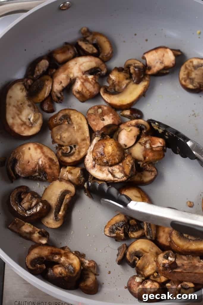 20-Minute Sautéed Zucchini and Mushrooms Recipe 7 sliced mushrooms being cooked in a gray pan.