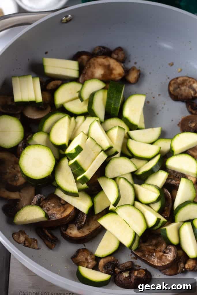 20-Minute Sautéed Zucchini and Mushrooms Recipe 8 sliced and cut zucchini in a pan with partially cooked sliced mushrooms.