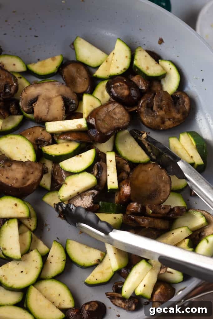 20-Minute Sautéed Zucchini and Mushrooms Recipe 9 sauteed mushrooms and zucchini in a gray pan being stirred with tongs.
