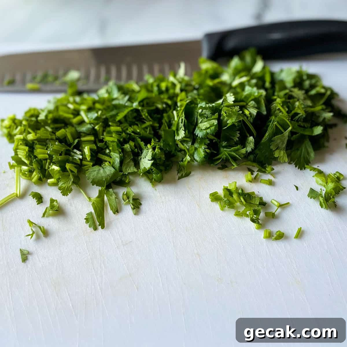Chopped fresh cilantro is shown on a white cutting board with a kitchen knife in the background.