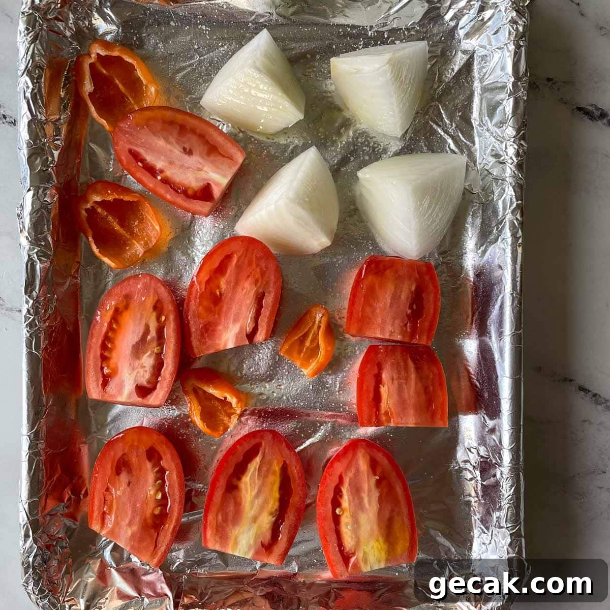 Halved tomatos and habaneros and half of a quartered white onion are shown a sheet tray covered with tin foil.