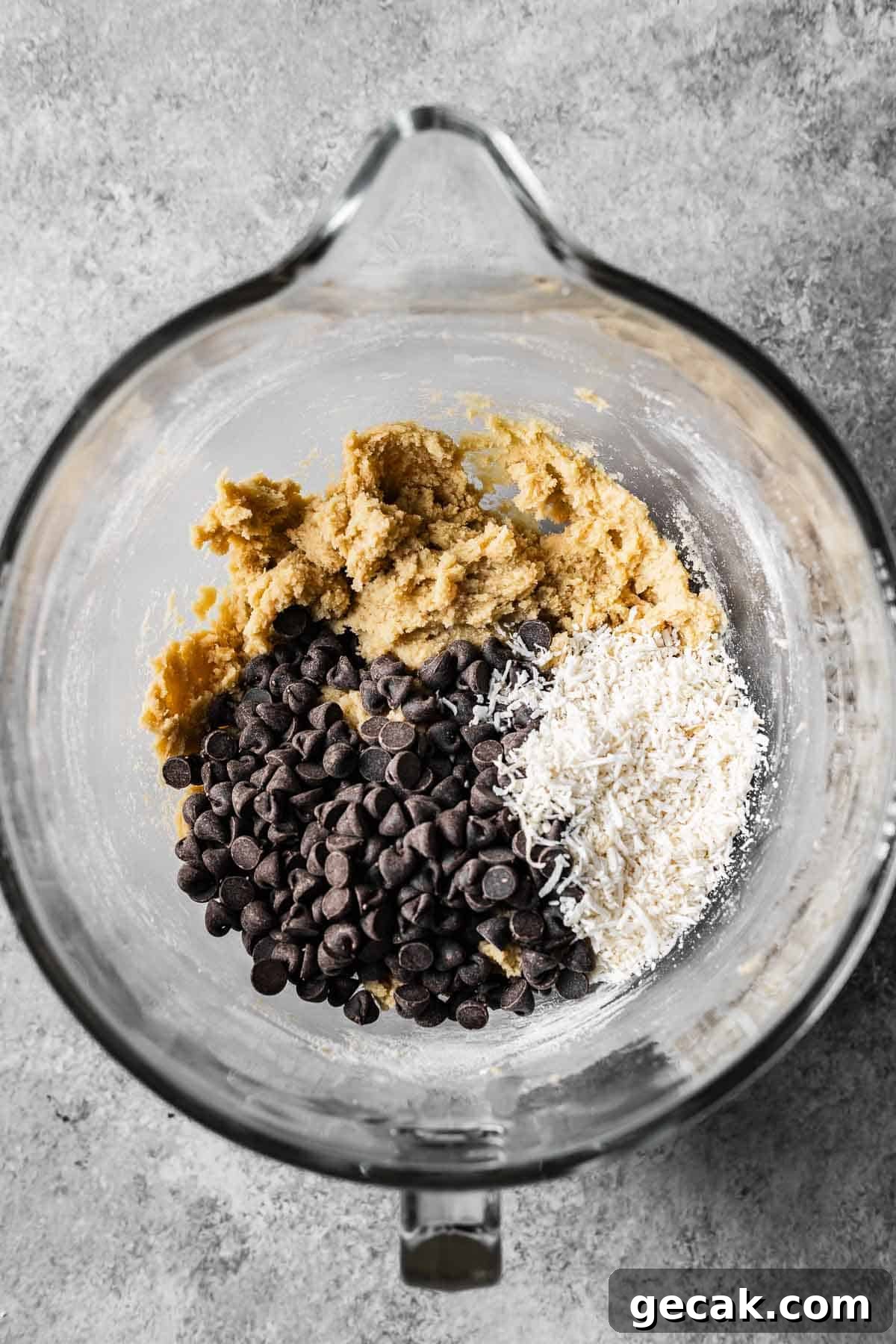 A mixing bowl with chocolate chips and shredded coconut on top of cookie dough.